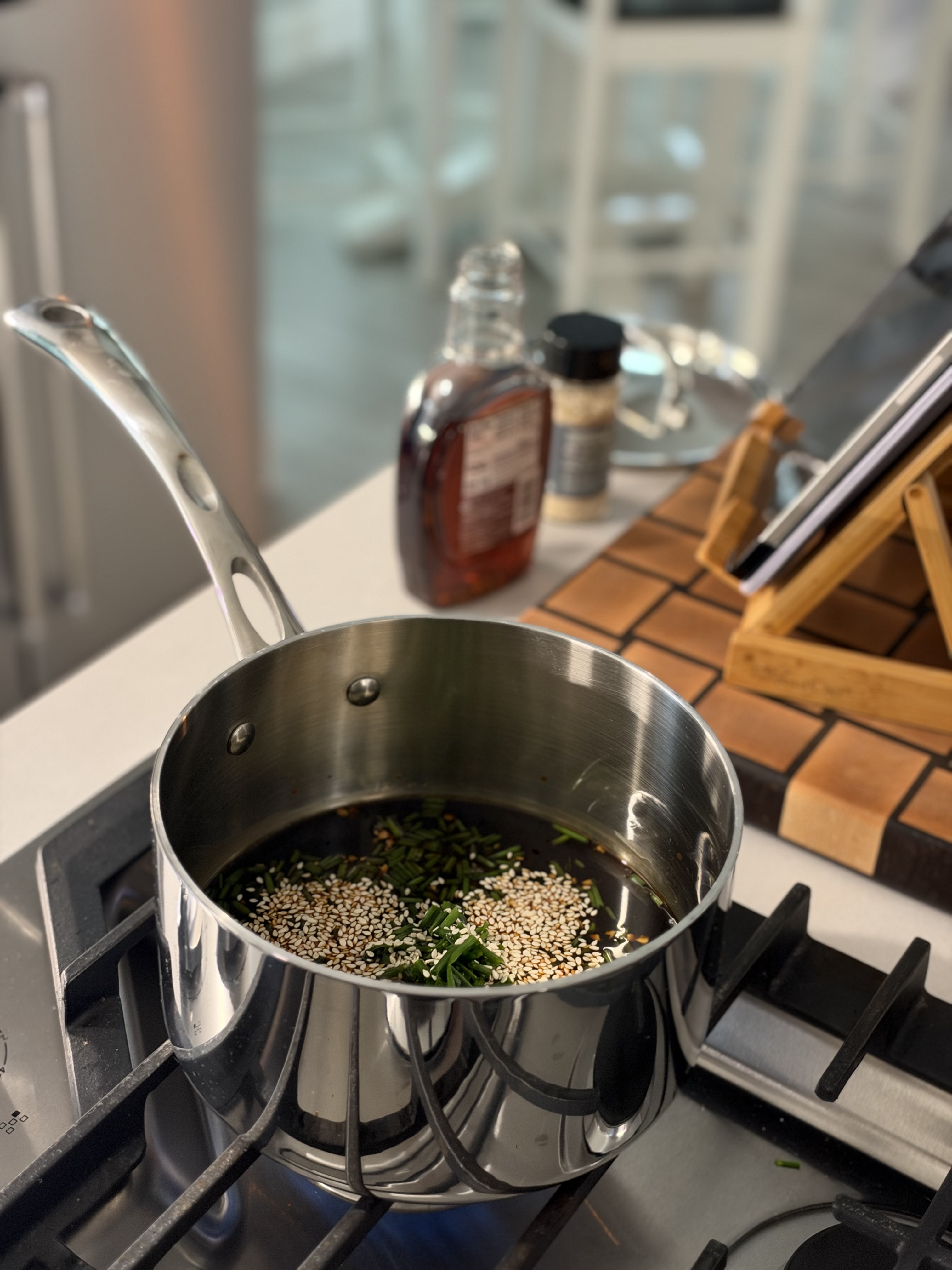 A small saucepan of glossy teriyaki sauce simmering with toasted sesame seeds and chopped chives